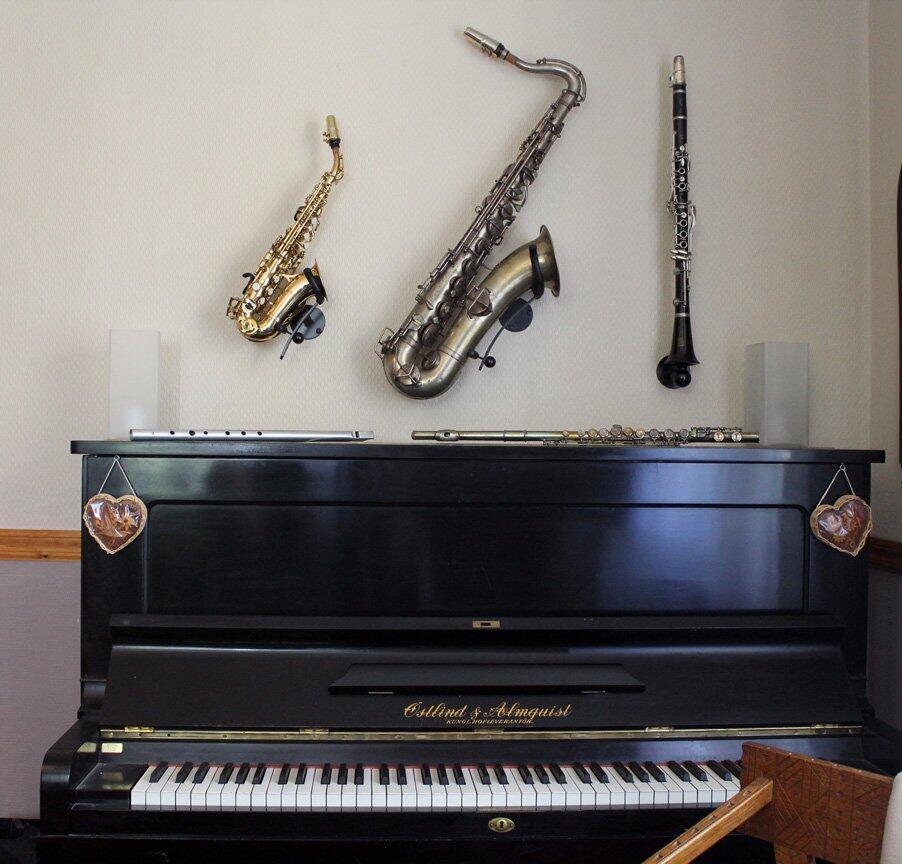 Piano with saxophone, clarinet, and flute on a wall above it