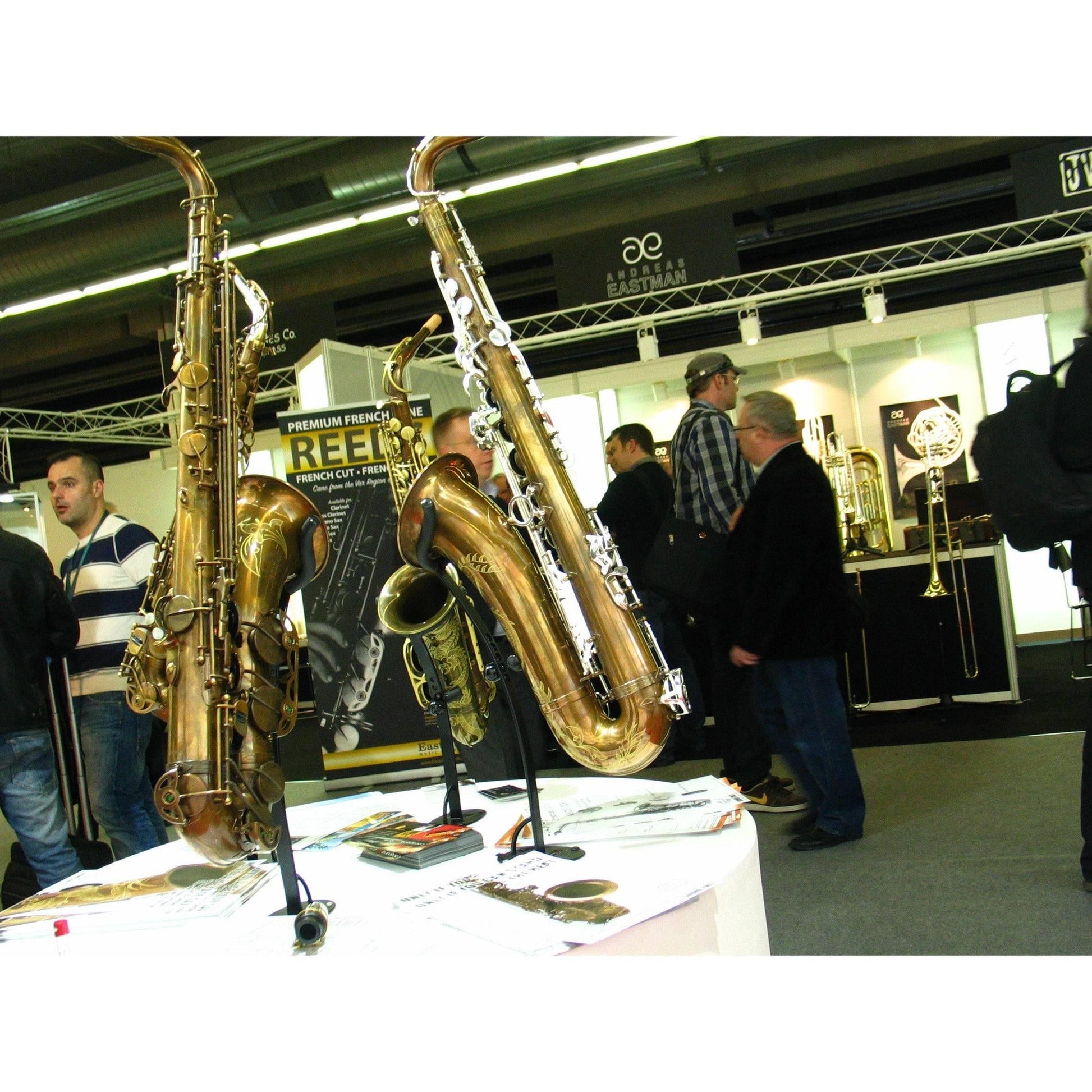 tradeshow visitors with 4 exhibit desktop tenor saxophone stands with instruments on display in the foreground by Locoparasaxo