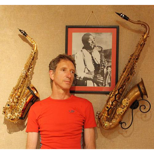 man in orange tee flanked by two saxophones in wall-mounted stands by Locoparasaxo